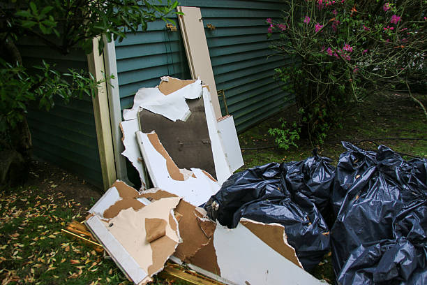 Broken pieces of wall and black bags are discarded near a green structure outdoors.