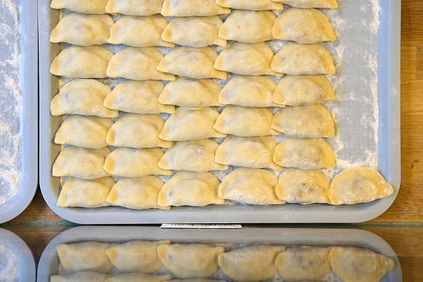 Close-up shot of a neatly sealed dumpling with sauerkraut and mushroom filling, held in a hand over a sheet of dough circles