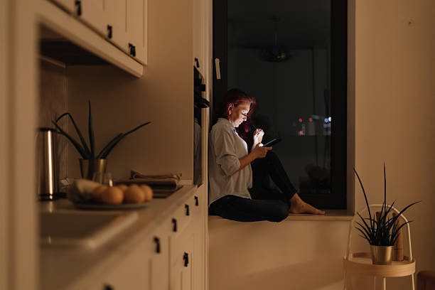 istock Woman sits in windowlight alone at night looking at glowing smartphone representing blue light at night digital intimacy and emotional solitude during evening scrolling routine in modern lifestyle 2221458922