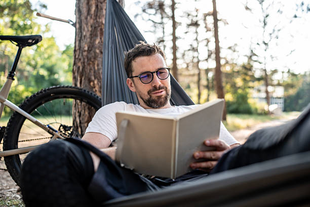 istock Man Relaxing In Hammock Reading Book Outdoors During A Sunny Day 2221460502