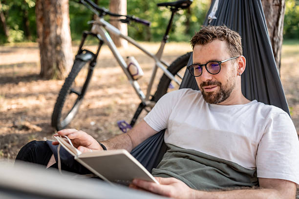 istock Man Relaxing in Hammock While Reading a Book Outdoors 2221460506