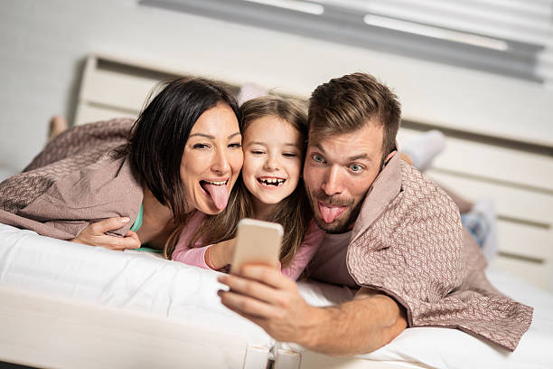 Family fun. Happy family taking selfie while lying on bed with funny facial expression. stock photo