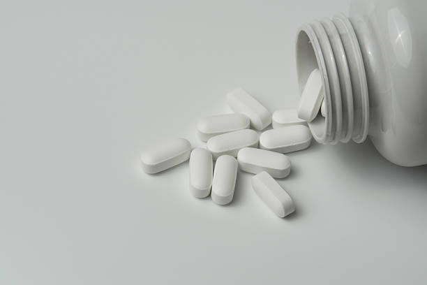 istock White pills tablets spilled from a bottle on a light grey background 2221462473