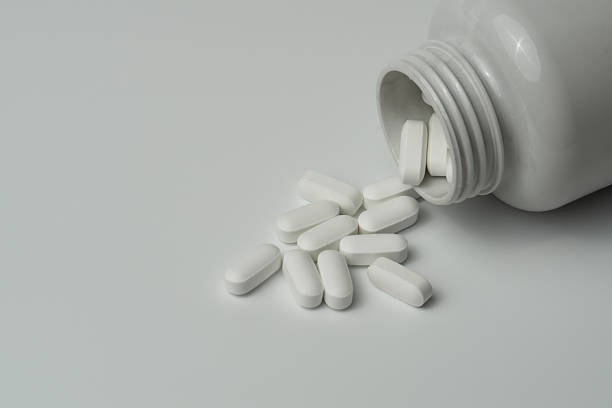 istock White pills tablets spilled from a bottle on a light grey background 2221462638