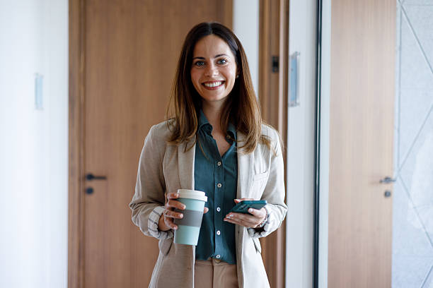 istock Professional businesswoman drinking takeaway coffee while checking smartphone in contemporary office corridor 2221468330