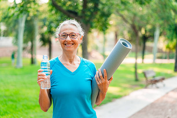 istock Outdoors senior woman taking a break, looking at camera holding a plastic water bottle, hydration, wellness and thirsty in a public park. Ederly person refresh with cold liquid on retirement workout 2221470396