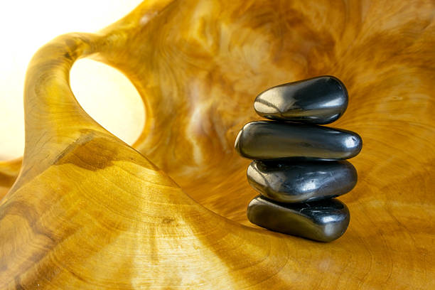 Stack of black stones on a wooden surface. The stones are arranged in a pyramid shape. Concept of balance and harmony, as the stones are stacked neatly on top of each other