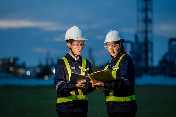 istock Two Engineers Working a Night Shift with a Laptop at an Industrial Plant. Two people wearing safety gear and holding papers 2221489074