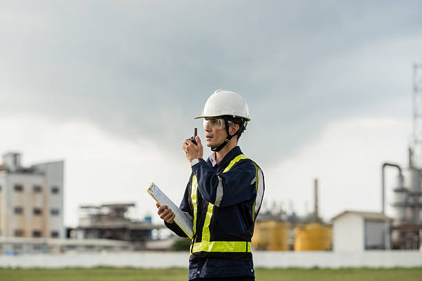 istock Site Supervisor Using a Walkie-Talkie for On-Site Communication. A man wearing a yellow vest and a hard hat is talking on a walkie talkie 2221489102