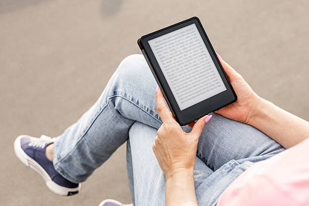 istock woman reading e-book sitting on bench, close-up. 2221493204