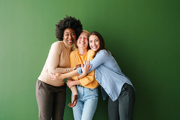 istock Three Multicultural Friends Hugging and Smiling Against a Bright Green Backdrop 2221495494