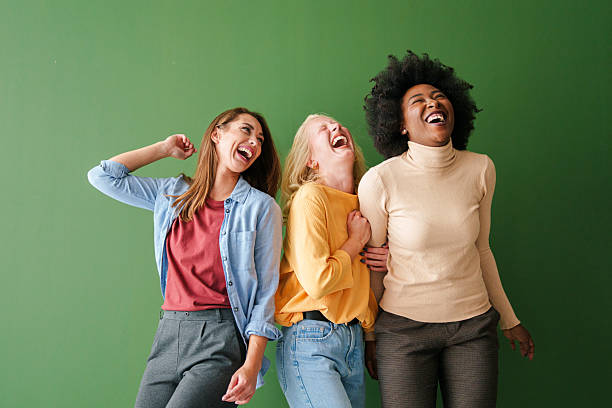 Three teenagers wearing funny Christmas clothes standing among gold confetti. Studio shot against green background.