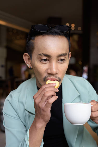 Portrait of nonbinary genderfluid young Asian gay man drinking coffee