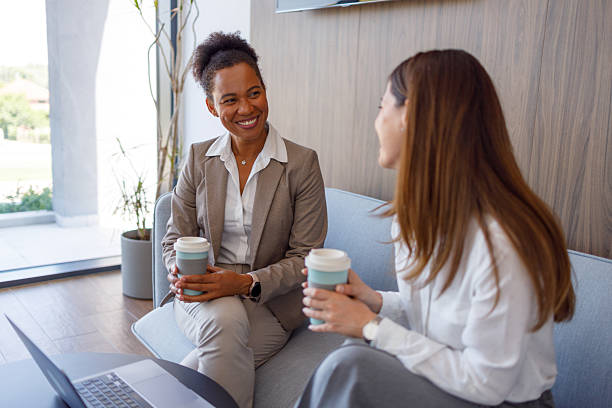 istock Professional women relaxing on sofa, sipping coffee and conversing animatedly during workplace break 2221505643