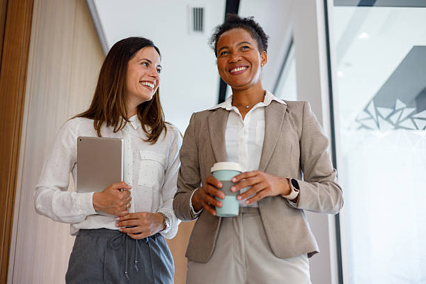 istock Professional women collaborating, navigating corporate workspace, tablet in hand, sharing coffee and conversation 2221510098