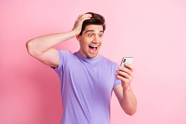 istock Portrait of nice cheerful amazed guy using gadget reading notification having fun isolated over pink pastel color background 2221516747