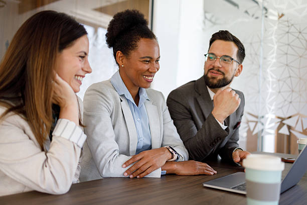 istock Three business people are sitting at a table, smiling and looking at a laptop during a productive meeting 2221517151