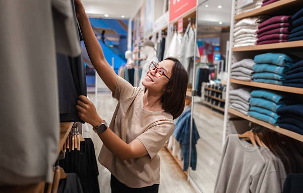 istock Young woman happily selecting clothes while browsing through organized shelves in a modern retail store, enjoying her shopping experience 2221520940