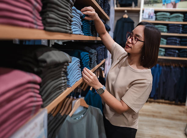 istock Asian customer browsing through a vibrant selection of colorful t-shirts while shopping for clothes in a bustling retail store 2221520943