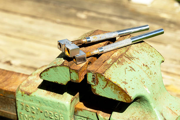 istock A rusty green vise holds two metal calipers on a wooden surface. The scene captures tools used for precision work in a workshop setting. 2221522734