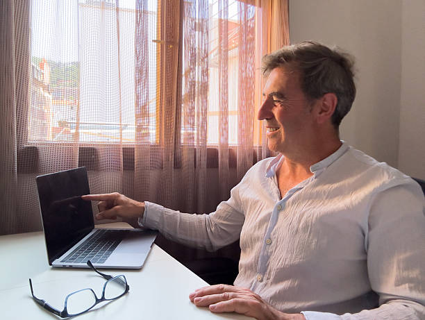 istock Smiling mature businessman pointing at laptop screen while working from home office 2221525320