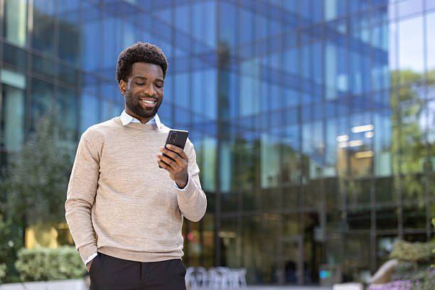 istock A stylish Black man smiles while using his smartphone in front of a glass office building. 2221534662