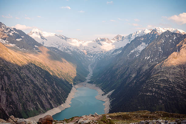 Alpine reservoir surrounded by snow-capped mountains at sunset