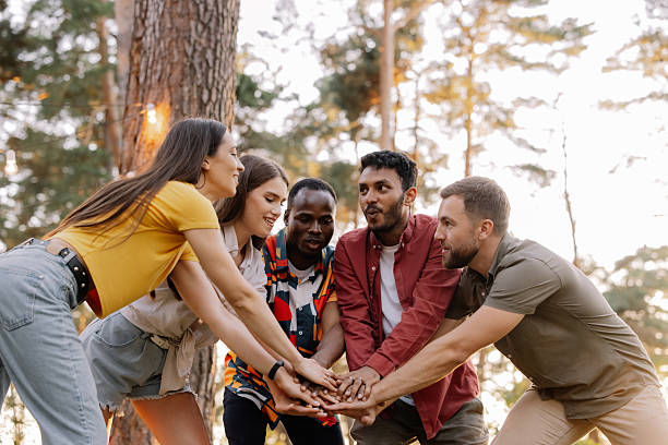 Interracial friends joining hands, symbolizing unity and teamwork, in the peaceful setting of a forest