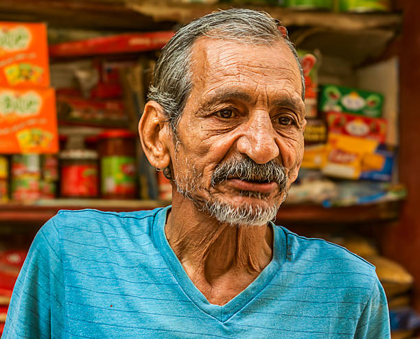 Cairo, Egypt – October 6, 2018: An elderly Egyptian man sitting inside a traditional street kiosk, surrounded by colorful snack and grocery products.