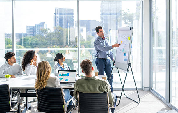 Business people watching a presentation on the whiteboard. A man is writing on the whiteboard with charts and graphs.