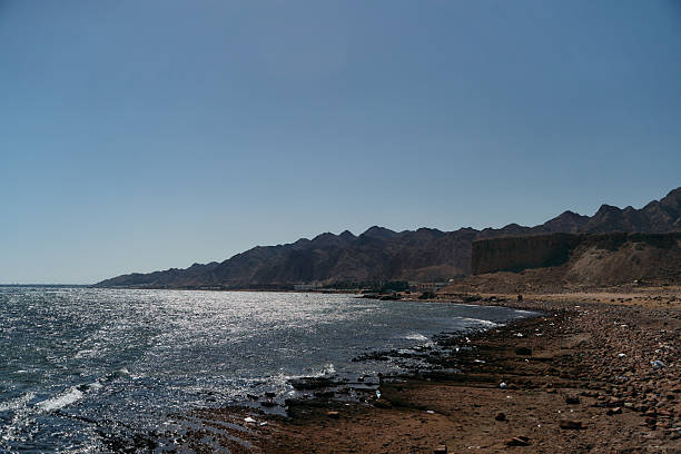A beautifully serene beach scene showcases majestic mountains and gentle waves under a clear, bright sky