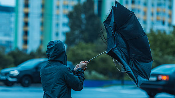 man with umbrella hiding from wind and rain. stormy weather - kuvvetli yağmur stok fotoğraflar ve resimler