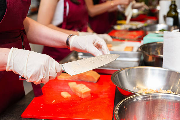 Group of people in a cooking class wearing gloves and aprons, slicing fresh salmon on red cutting boards with stainless bowls.