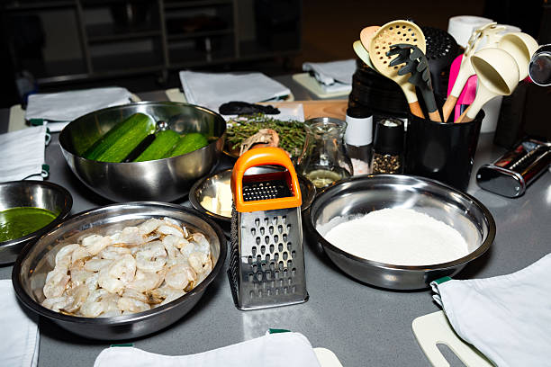 A kitchen countertop with fresh shrimp, zucchini, flour, herbs, and cooking tools prepared for a gourmet cooking session.