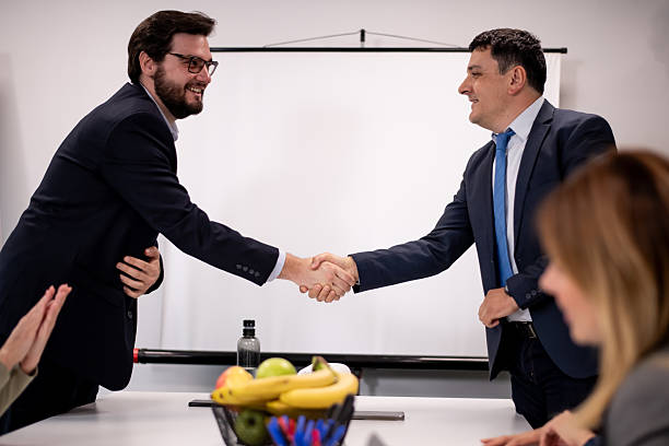 istock Two executives shaking hands during a business meeting in a modern office setting with colleagues observing, symbolizing collaboration, agreement, and professionalism in a professional work environment. 2221564355