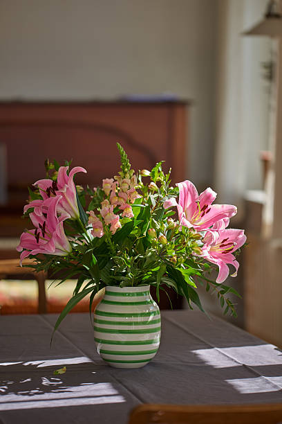 Close-up of Alstroemeria flowers in a pot by the window, commonly known as Peruvian lilies or Lily of the Incas. The petals are pale pink with darker streaks, and the background consists of blurred greenery and other flowers, enhancing the focal point's delicate beauty.