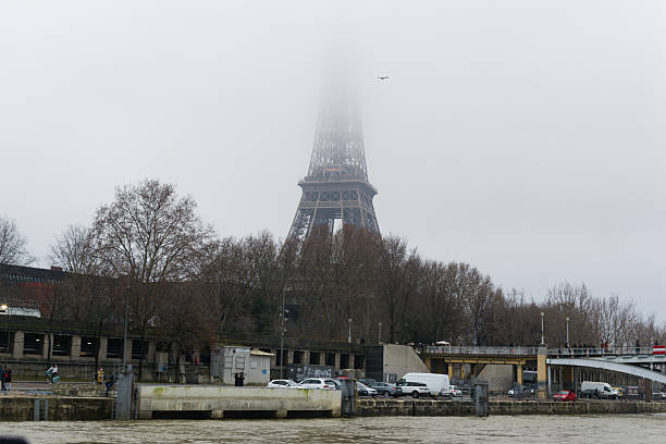 Paris, France â January 01, 2020: Iconic tower shrouded in fog rises behind the river. Editorial image captures a mood. Useful for travel, weather, or architecture stories.