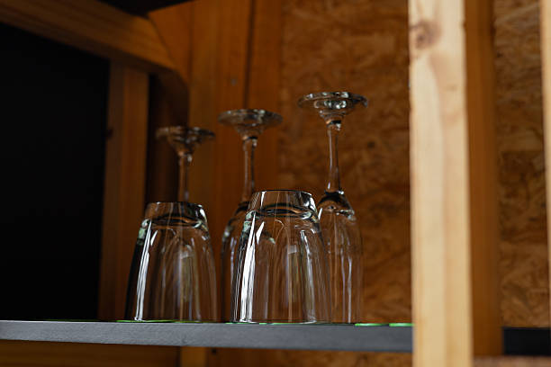 Transparent glasses and delicate wine cups sit in perfect order on a rustic wooden shelf, blending functionality and style in the cozy setting of the glamping area.