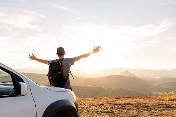 Joyful man with arms wide open on top of a car at sunset. A moment of freedom, inspiration, and celebration during a road trip.