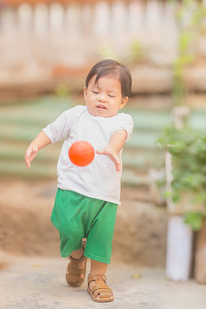 A young child is playing with a red ball. The child is wearing a white shirt and green shorts