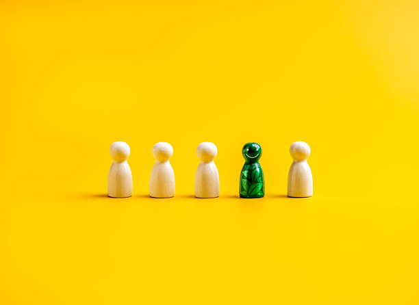 istock Green people. Business with environmental conservation and responsibility concept. Leaf graphic pattern on green peg doll people figures, different from other whites, on yellow background, minimalist. 2221582532