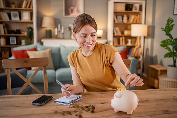 istock Woman saving money at home using piggy bank and notebook 2221584991