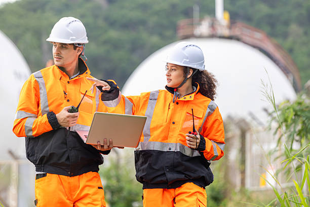 istock Engineers Collaborating at Industrial Site with Storage Tanks, Team of Engineers Conducting Operations at Oil Storage Field Industrial Site, Industrial Workers Communicating and Using Laptop at Site 2221586098