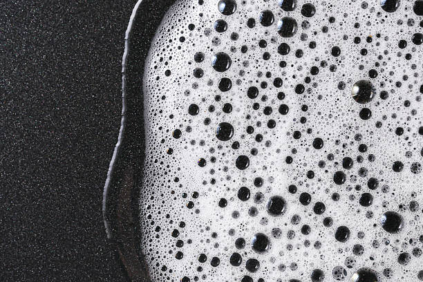 istock Soap foam with bubbles on black surface. Abstract cleaning concept. Hygiene and disinfection theme. Closeup of suds texture. 2221595448