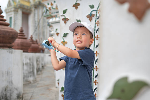 istock Boy in white hat exploring Wat Arun temple in Bangkok Thailand courtyard with camera 2221596817