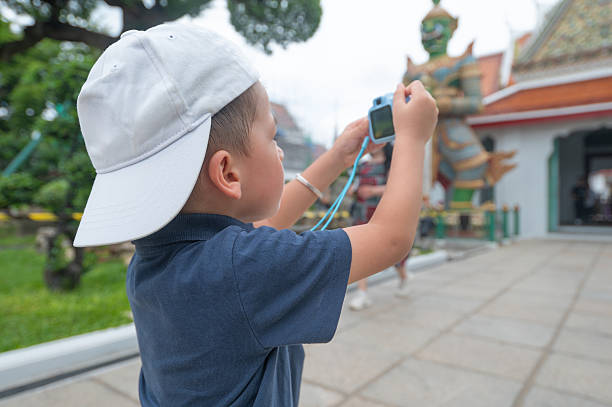 Boy in white hat exploring Wat Arun temple in Bangkok Thailand courtyard with camera