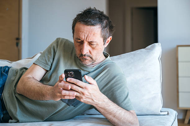 istock Bored couch potato guy using mobile phone while laying on living room sofa 2221597812