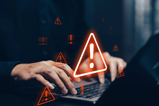 istock Digital cybersecurity alert with glowing orange warning signs overlaying a person's hands holding a smartphone and laptop in a dark, tech-focused environment. This powerful conceptual image illustrates online threats, data breach risks, cybercrime. 2221601367