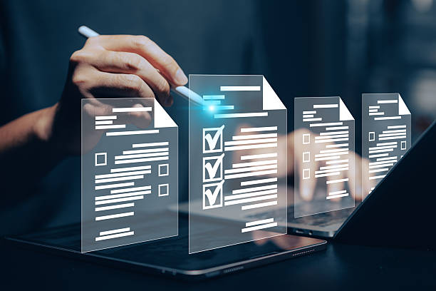 istock Digital document checklist and online form completion: Close-up of a hand using a stylus on a tablet to interact with holographic checklist boxes and digital document icons above a laptop. This conceptual image illustrates online surveys, digital forms. 2221601934