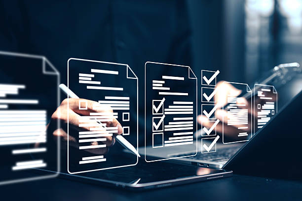 istock Digital document checklist and online form completion: Close-up of a hand using a stylus on a tablet to interact with holographic checklist boxes and digital document icons above a laptop. This conceptual image illustrates online surveys, digital forms. 2221601954